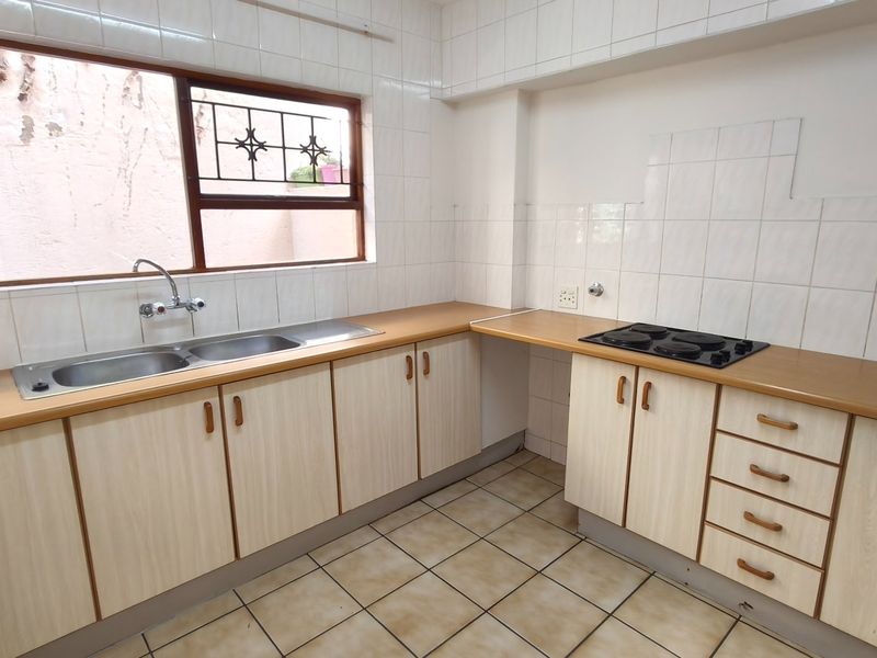 A functional kitchen featuring laminate countertops, built-in cabinetry, a double basin sink, and an electric hob with tiled splashbacks.