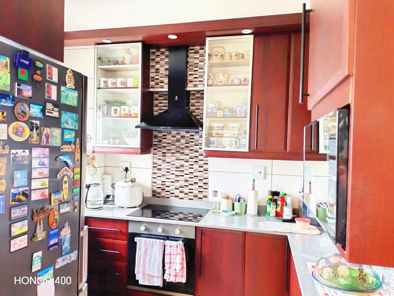 A functional kitchen featuring dark wood cabinetry, a mosaic tile splashback, integrated oven and hob, and stone countertops.