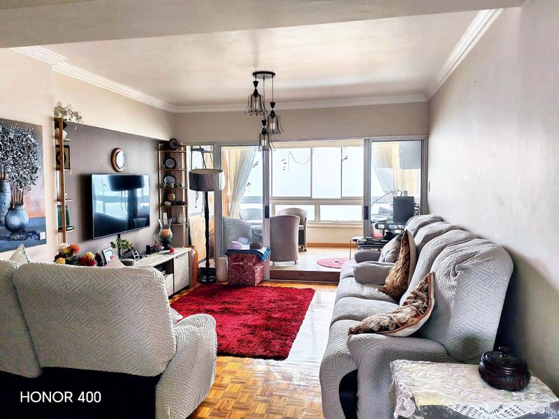 A comfortable living room featuring classic parquet flooring, crown molding, and large sliding glass doors that provide access to an adjoining balcony area.