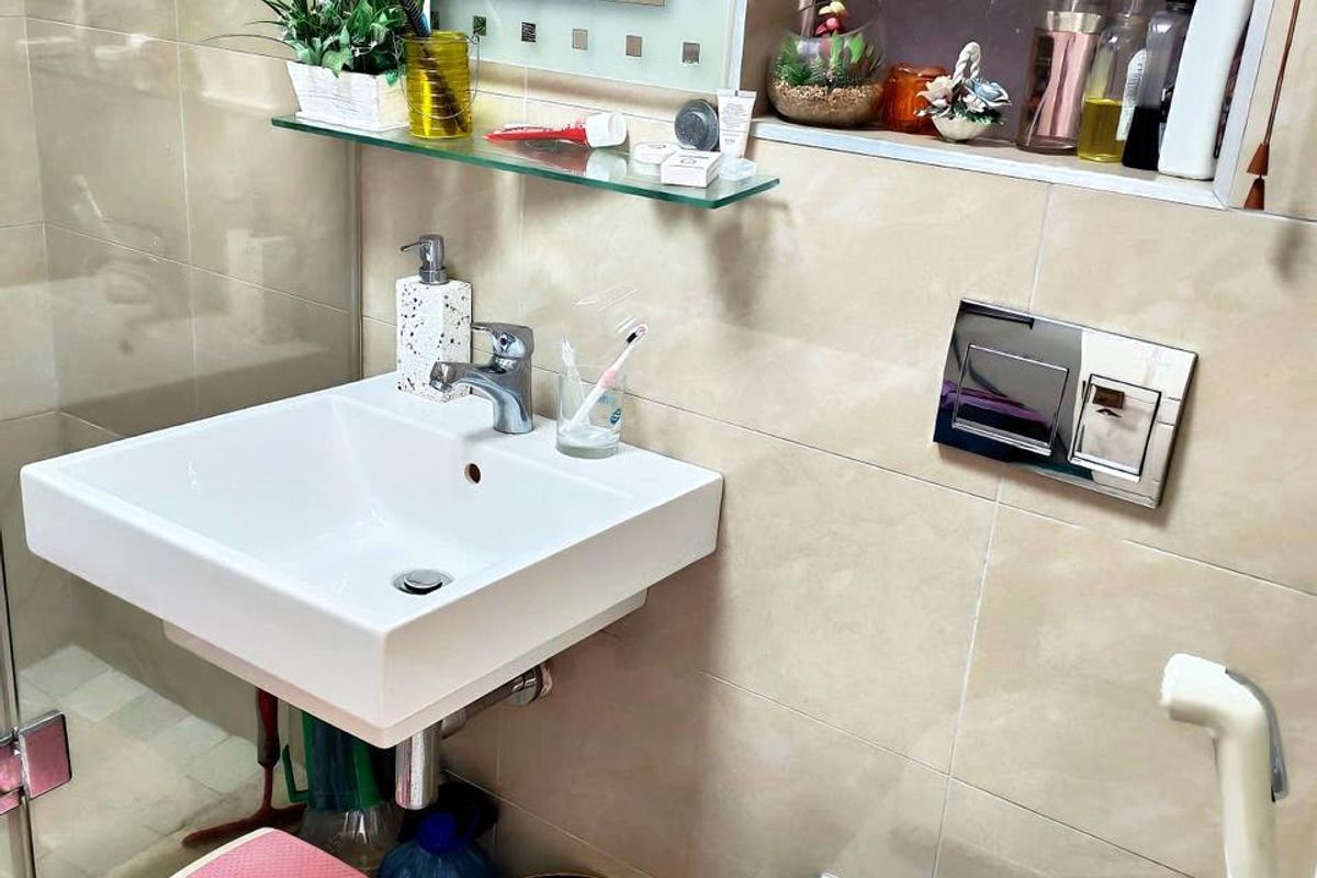A compact bathroom featuring a wall-mounted basin, wall-hung toilet with chrome flush plate, and a glass shower enclosure with tiled finishes.