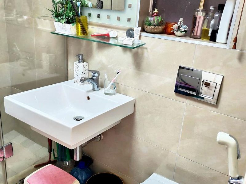 A compact bathroom featuring a wall-mounted basin, wall-hung toilet with chrome flush plate, and a glass shower enclosure with tiled finishes.
