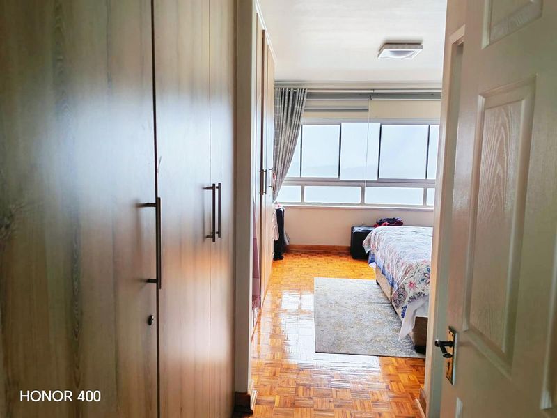 A bedroom featuring parquet flooring, extensive built-in cupboards, and a large window providing natural light and exterior views.