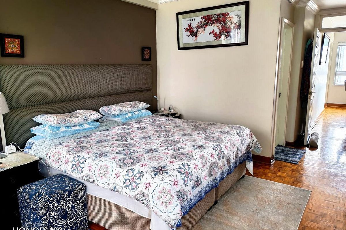 A well-maintained bedroom featuring classic parquet flooring, crown molding, and a built-in headboard, offering a comfortable and functional living space.