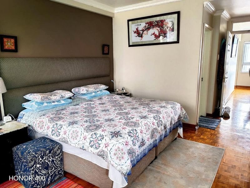 A well-maintained bedroom featuring classic parquet flooring, crown molding, and a built-in headboard, offering a comfortable and functional living space.