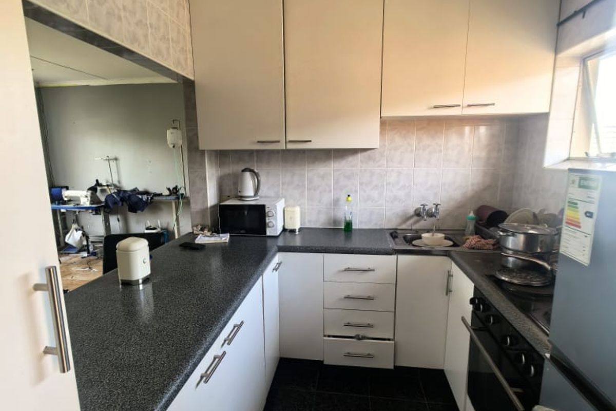 A functional kitchen featuring white cabinetry, dark laminate countertops, built-in oven, hob, and tiled finishes, offering a practical layout for daily meal preparation.