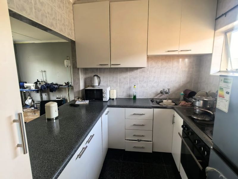 A functional kitchen featuring white cabinetry, dark laminate countertops, built-in oven, hob, and tiled finishes, offering a practical layout for daily meal preparation.