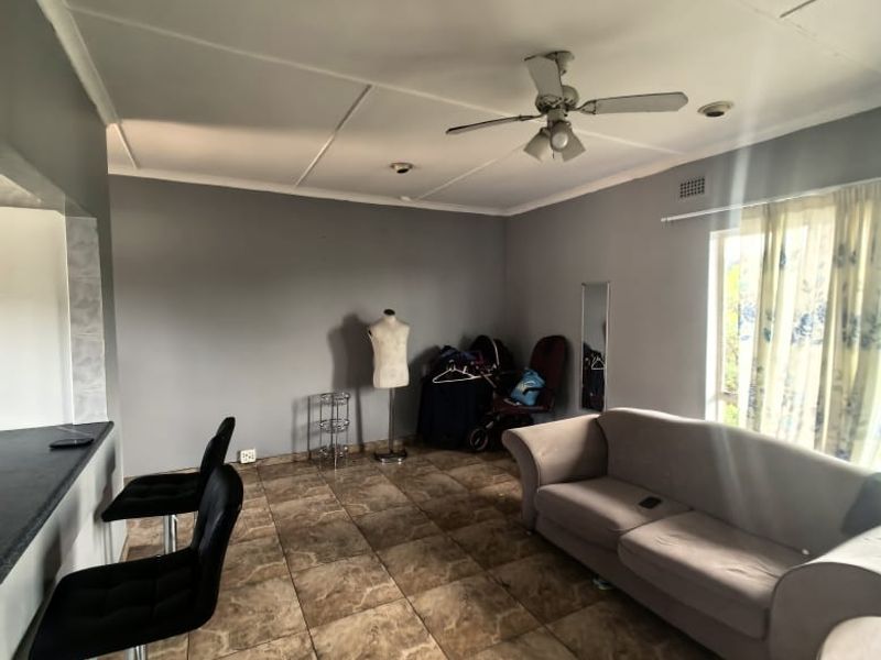 Open plan living area featuring tiled flooring, a breakfast bar, and a ceiling fan, offering a functional layout for daily living.
