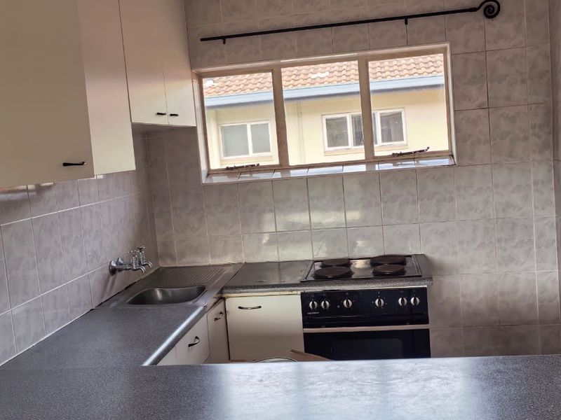 A functional kitchen featuring laminate countertops, built-in cabinetry, a stainless steel sink, and an integrated electric oven and hob with tiled splashbacks.