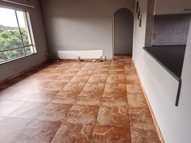 An open-plan living area featuring tiled flooring, a ceiling fan, and a breakfast bar connecting to the kitchen space.