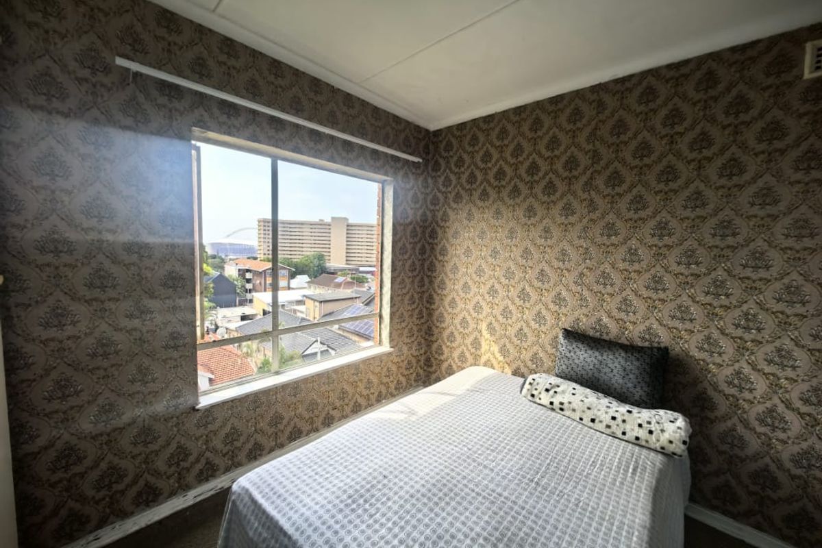 A bedroom featuring patterned wallpaper and a large window with an urban view, offering potential for modernization through updated finishes.