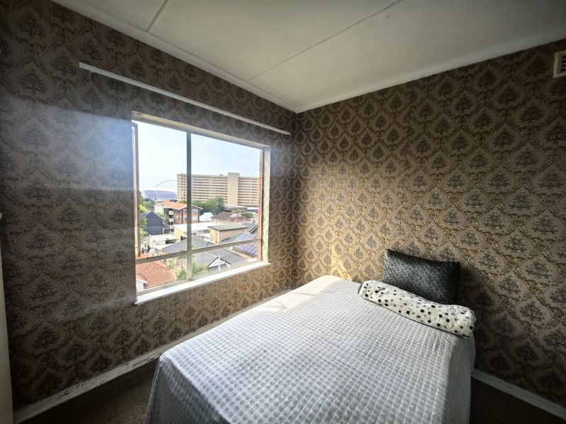 A bedroom featuring patterned wallpaper and a large window with an urban view, offering potential for modernization through updated finishes.