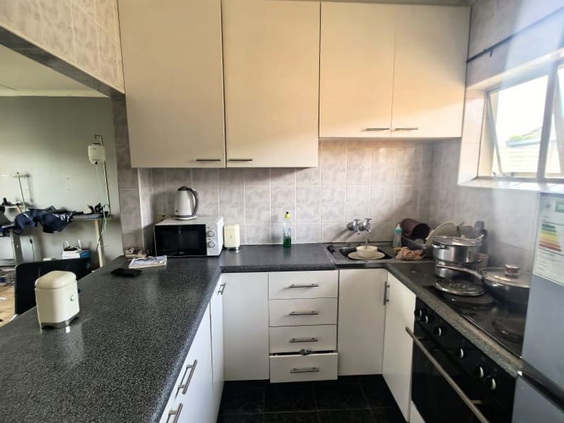 A functional kitchen featuring white cabinetry, dark laminate countertops, a built-in electric oven and hob, and tiled finishes throughout.