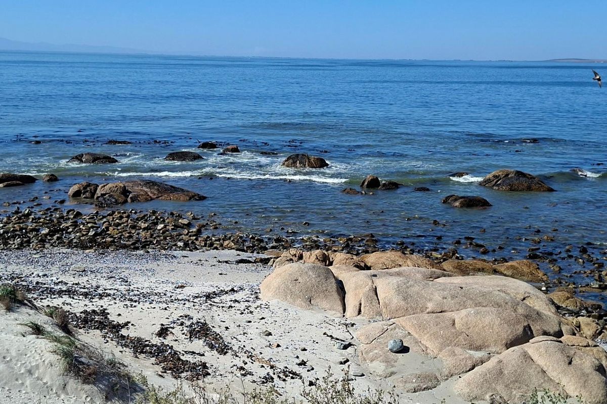 A scenic view of the ocean coastline featuring a rocky shoreline and sandy beach area.