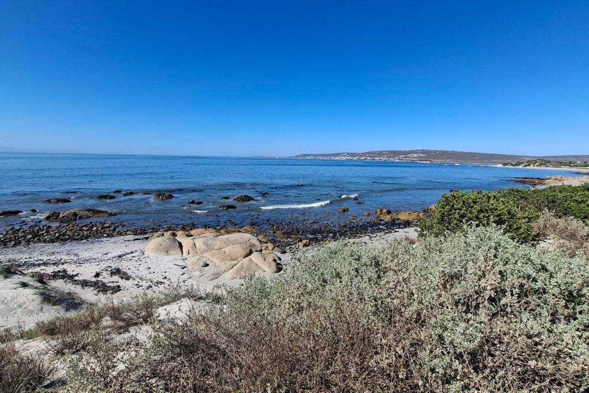 A scenic view of the coastal landscape featuring a sandy beach, rocky shoreline, and clear ocean waters.