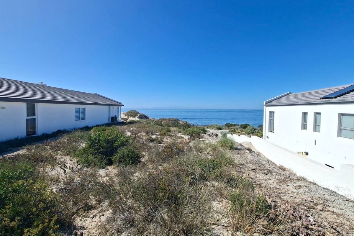 Rear view of the property showing two white residential structures with tiled roofs, situated on a coastal plot with direct ocean views.