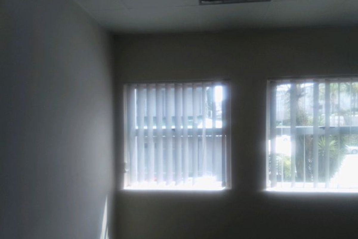 An empty office space featuring neutral walls, recessed ceiling lighting, and vertical window blinds.