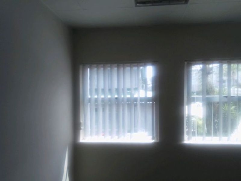 An empty office space featuring neutral walls, recessed ceiling lighting, and vertical window blinds.