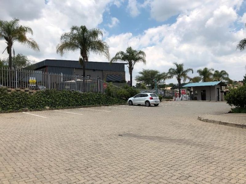 Commercial property exterior featuring a paved parking area, security fencing, and a dedicated guard house structure.