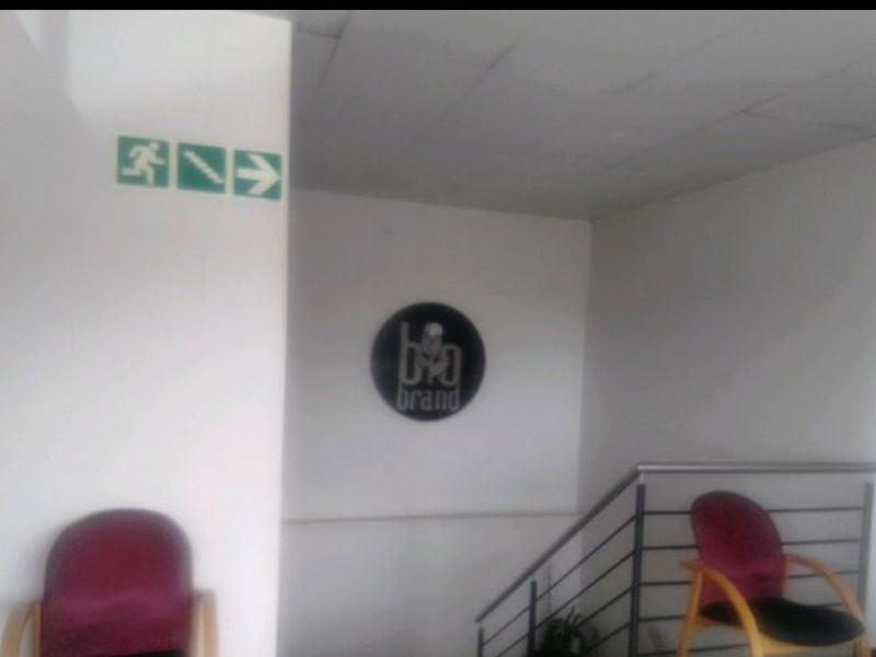 A commercial hallway featuring a staircase with a metal handrail, suspended ceiling tiles, and emergency exit signage.