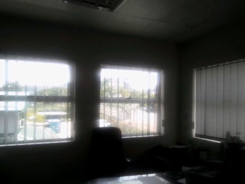 A commercial office space featuring multiple windows with vertical blinds and security bars, providing natural light and exterior views.