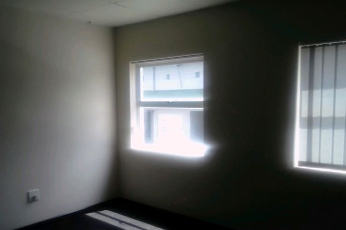 An empty, functional office space featuring a suspended ceiling, neutral walls, and windows fitted with vertical blinds.