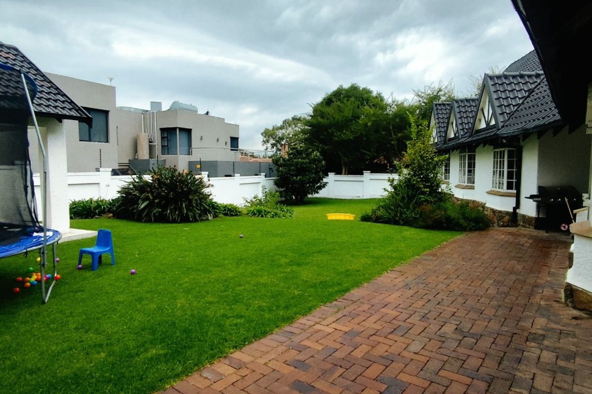 A spacious rear garden featuring a paved brick patio, well-maintained lawn, and perimeter boundary walls, providing a private outdoor area.