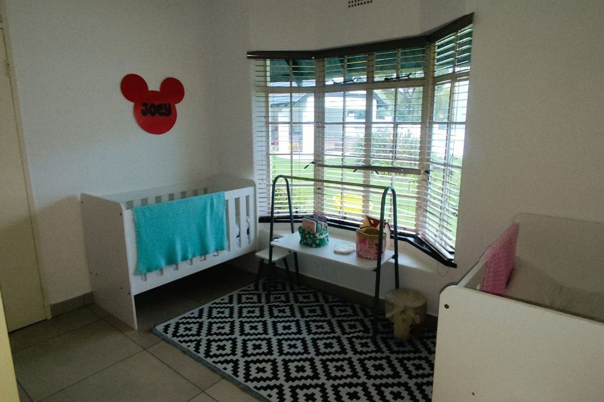 A bedroom featuring tiled flooring and a large bay window with fitted blinds, providing natural light and views of the exterior.
