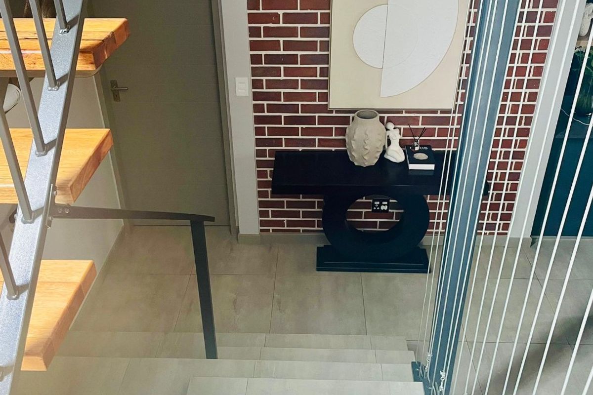 A modern hallway featuring a staircase with timber treads, a striking exposed brick feature wall, and contemporary tiled flooring.