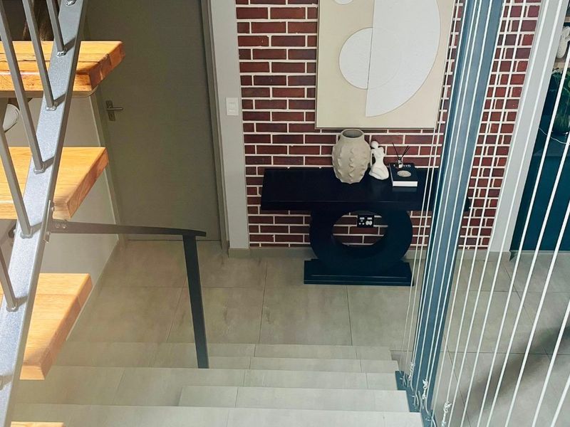 A modern hallway featuring a staircase with timber treads, a striking exposed brick feature wall, and contemporary tiled flooring.