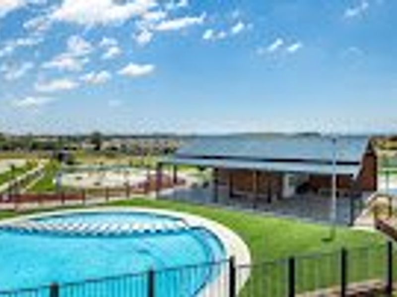 An outdoor pool area featuring a swimming pool, a covered patio structure with a metal roof, and surrounding landscaped garden space.