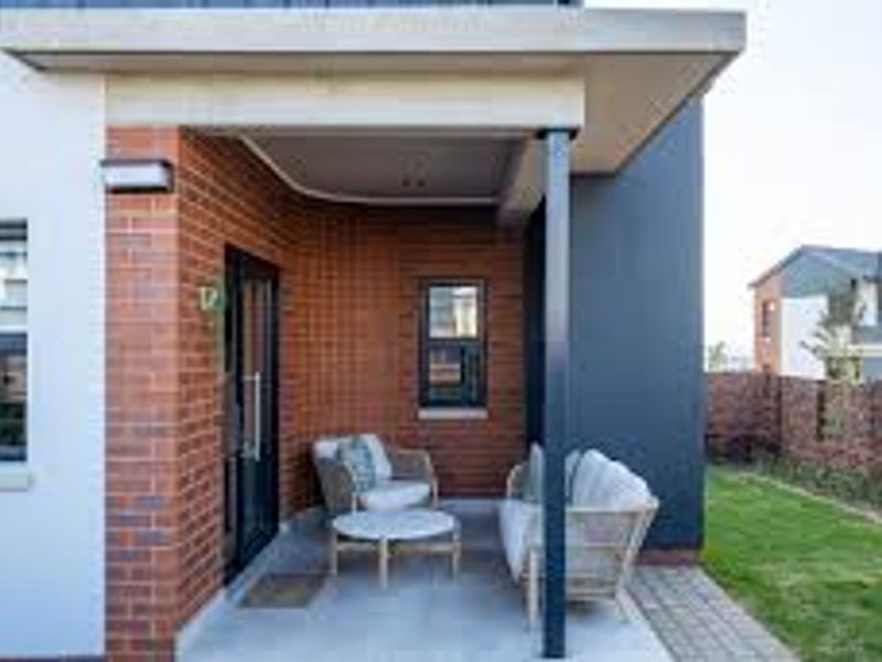 A modern covered patio area featuring brick detailing, concrete flooring, and recessed lighting, providing a seamless transition to the adjacent garden space.