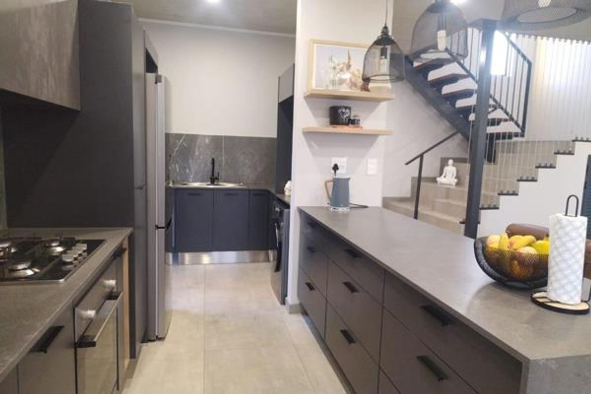 Modern kitchen featuring dark cabinetry, stone countertops, integrated appliances, and a sleek staircase leading to the upper level.
