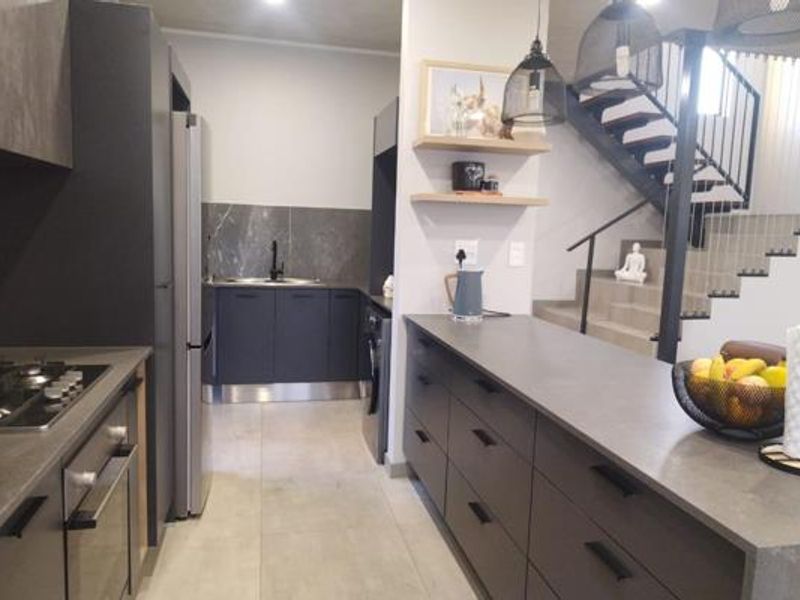 Modern kitchen featuring dark cabinetry, stone countertops, integrated appliances, and a sleek staircase leading to the upper level.