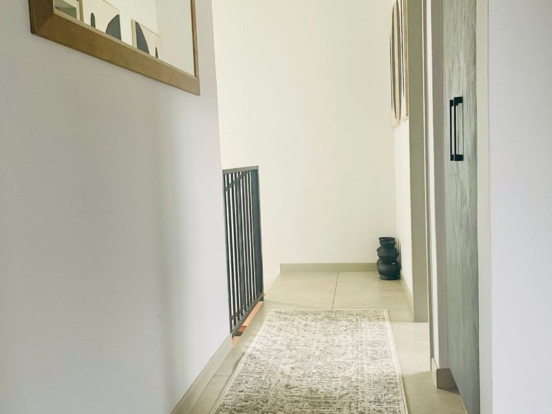 A bright and modern hallway featuring clean tiled flooring and a sleek metal balustrade, leading to adjacent living spaces.