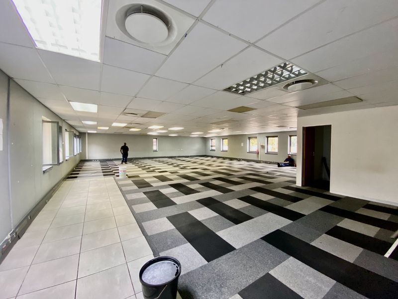 A large, open-plan commercial office space featuring a suspended ceiling, recessed lighting, and a mix of carpet and ceramic tile flooring.