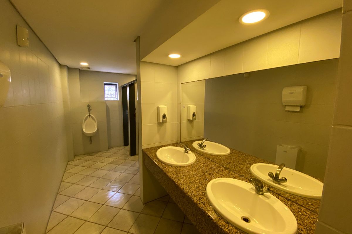 Commercial bathroom featuring a granite vanity with dual basins, large wall mirror, tiled finishes, and a separate urinal area.