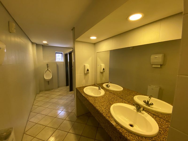 Commercial bathroom featuring a granite vanity with dual basins, large wall mirror, tiled finishes, and a separate urinal area.