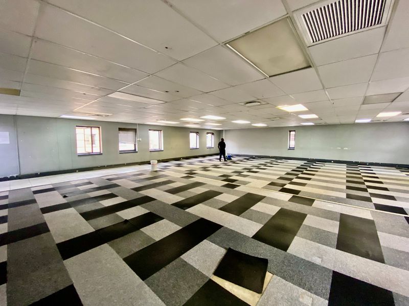 Spacious open-plan commercial office area featuring a suspended ceiling, recessed lighting, air conditioning, and patterned carpet tiles throughout.