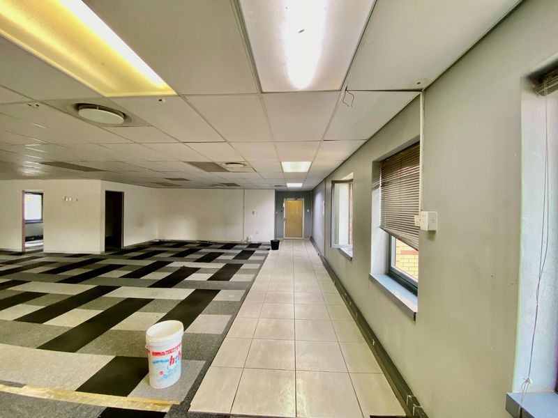 An open-plan commercial office space featuring a mix of carpet and tile flooring, suspended ceilings with recessed lighting, and large windows with blinds.