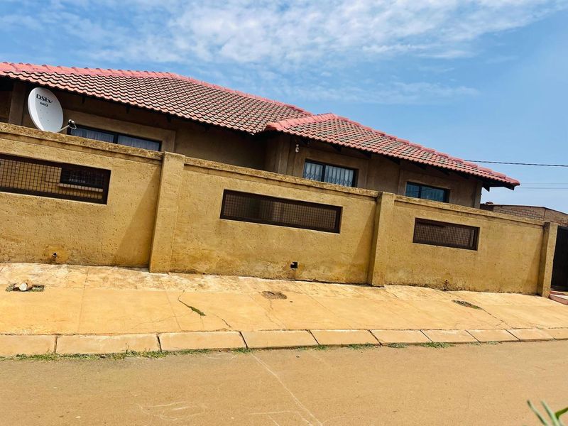 Front exterior view of the property featuring a tiled roof, perimeter wall with security inserts, and paved sidewalk area.