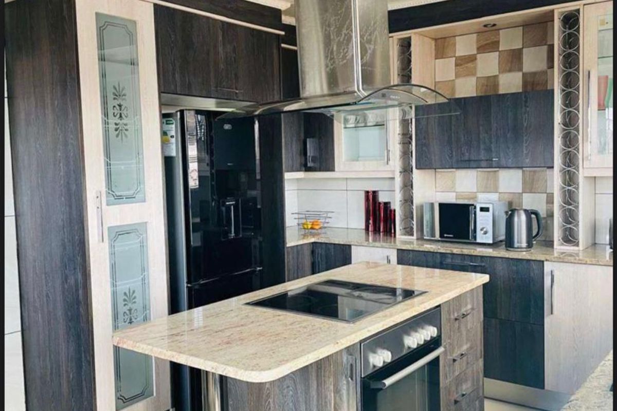 Modern kitchen featuring a central island with built-in oven and cooktop, granite countertops, dark wood cabinetry, and a stainless steel extractor fan.