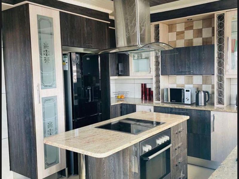 Modern kitchen featuring a central island with built-in oven and cooktop, granite countertops, dark wood cabinetry, and a stainless steel extractor fan.