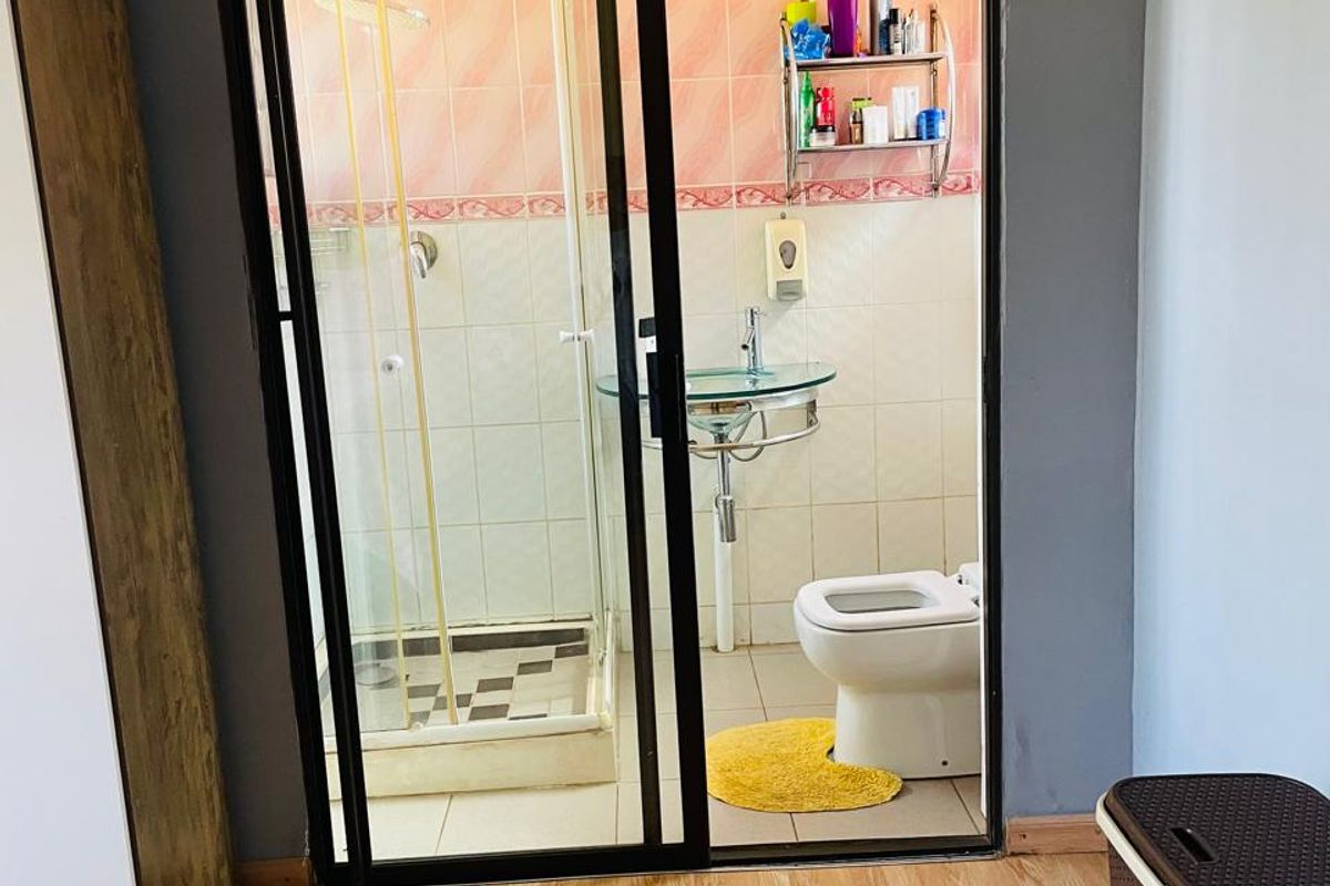 A compact bathroom featuring a glass shower enclosure, pedestal washbasin, and toilet, with dated wall tiling and a sliding door entry.