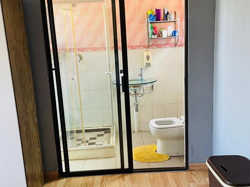 A compact bathroom featuring a glass shower enclosure, pedestal washbasin, and toilet, with dated wall tiling and a sliding door entry.