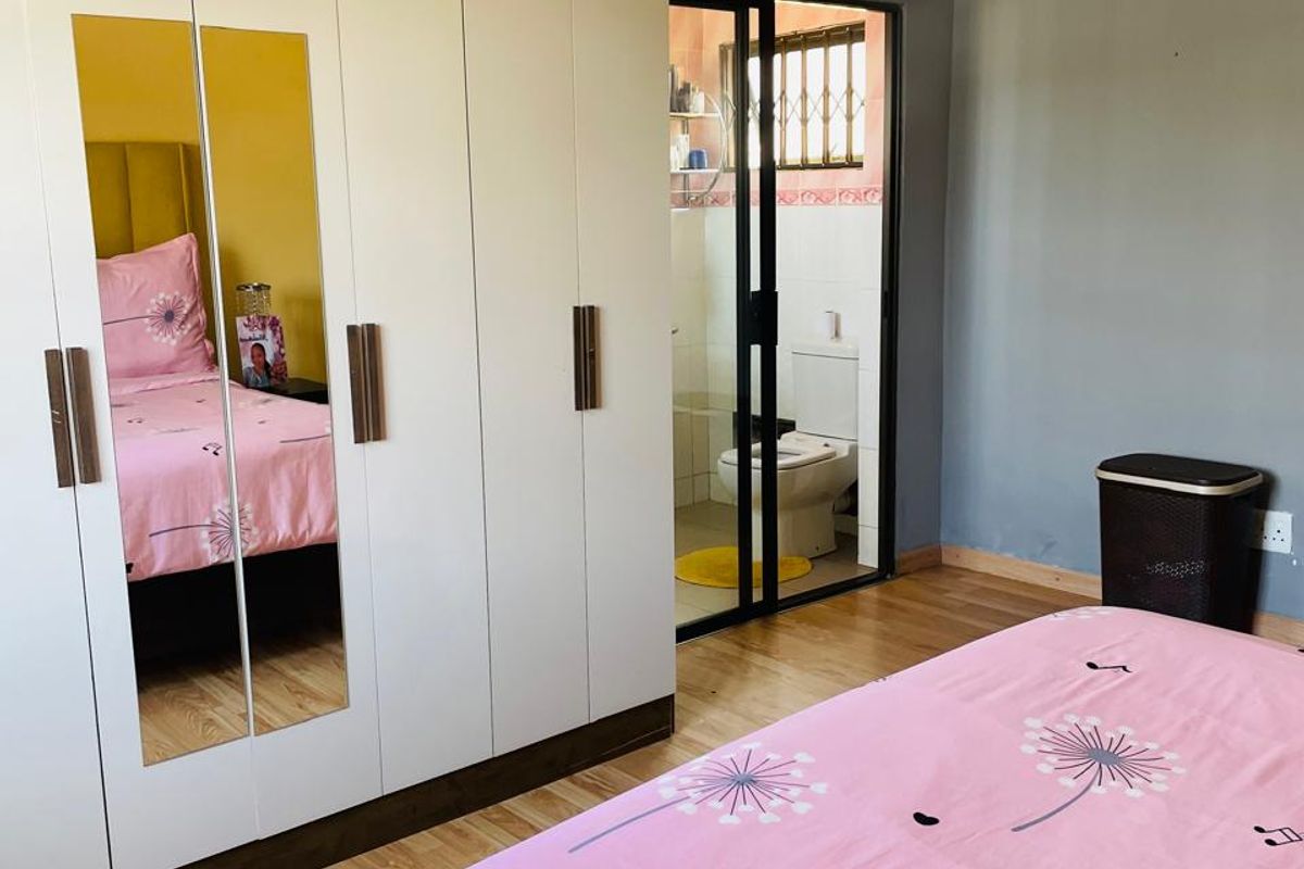 A bedroom featuring laminate flooring, a large built-in wardrobe with mirrored panels, and an adjoining en-suite bathroom with a sliding door entrance.