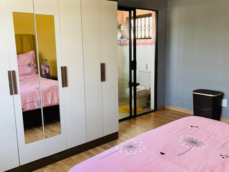 A bedroom featuring laminate flooring, a large built-in wardrobe with mirrored panels, and an adjoining en-suite bathroom with a sliding door entrance.