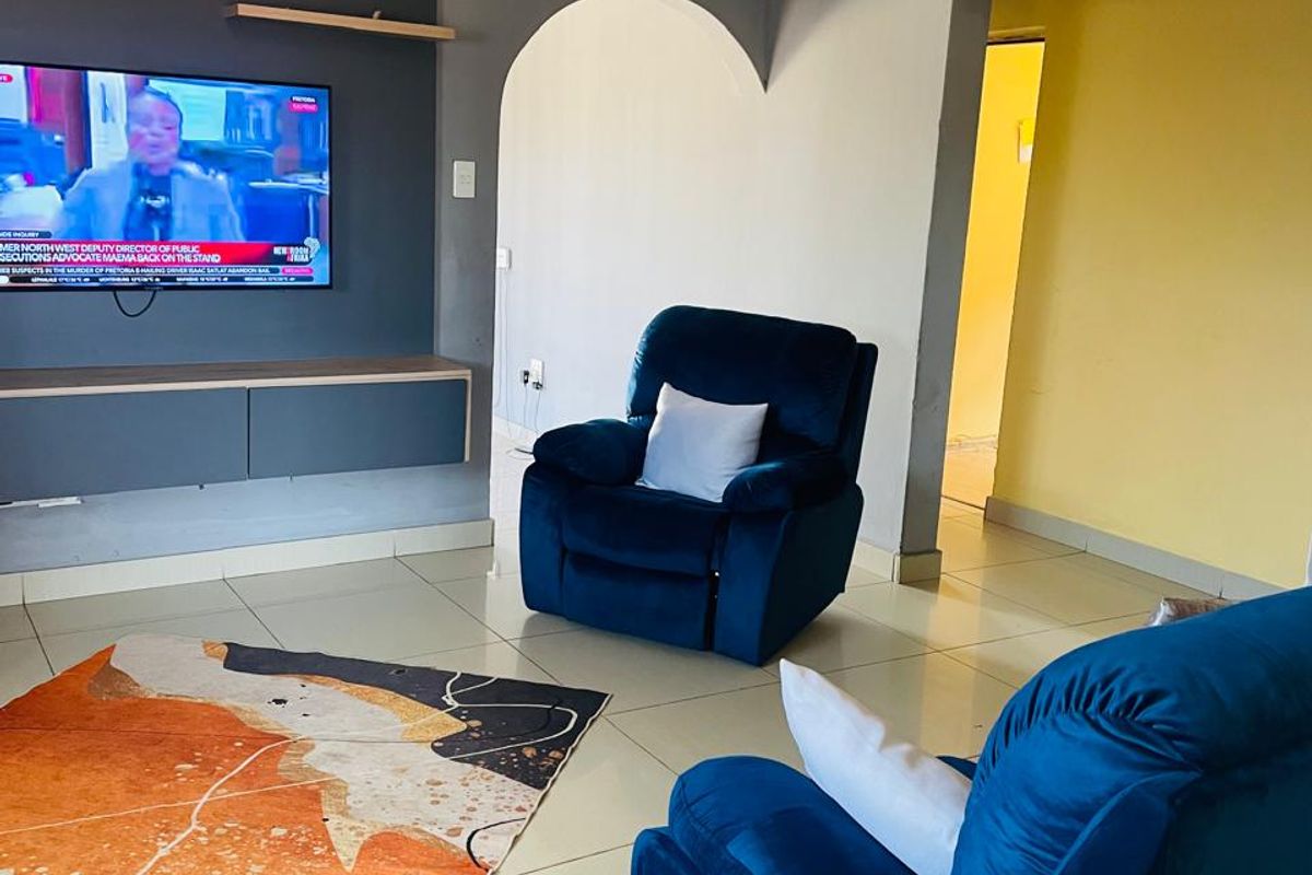 A living room featuring a built-in media console with floating shelves, tiled flooring, and a decorative arched doorway leading to an adjacent space.
