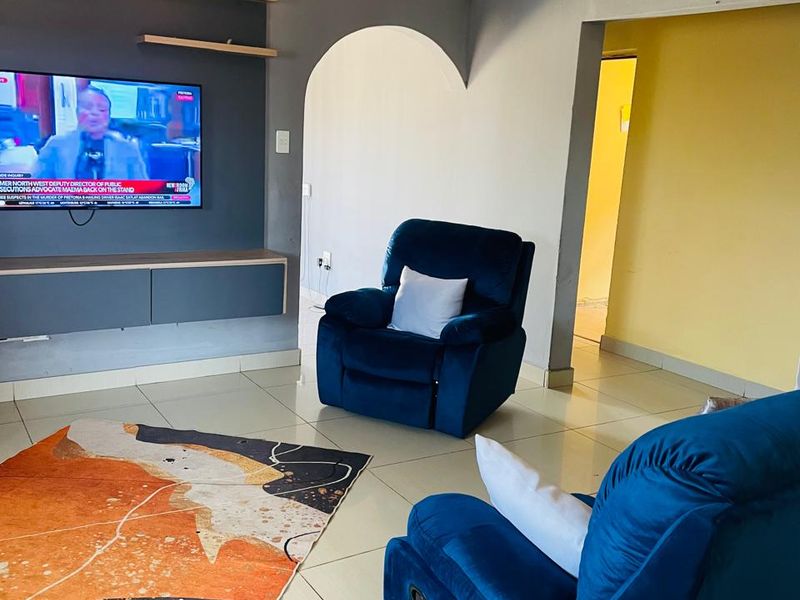 A living room featuring a built-in media console with floating shelves, tiled flooring, and a decorative arched doorway leading to an adjacent space.