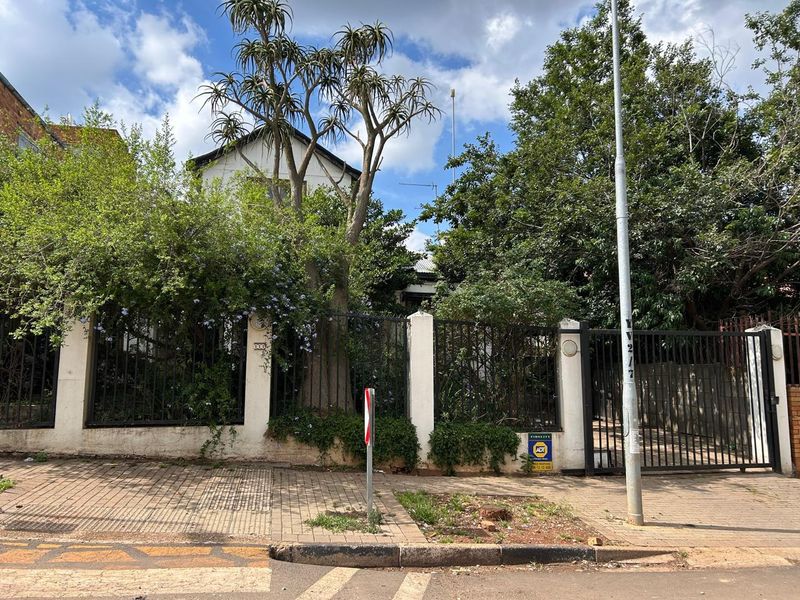 Front elevation of the property featuring a secure wrought iron fence, masonry pillars, and a metal driveway gate, partially obscured by mature trees.