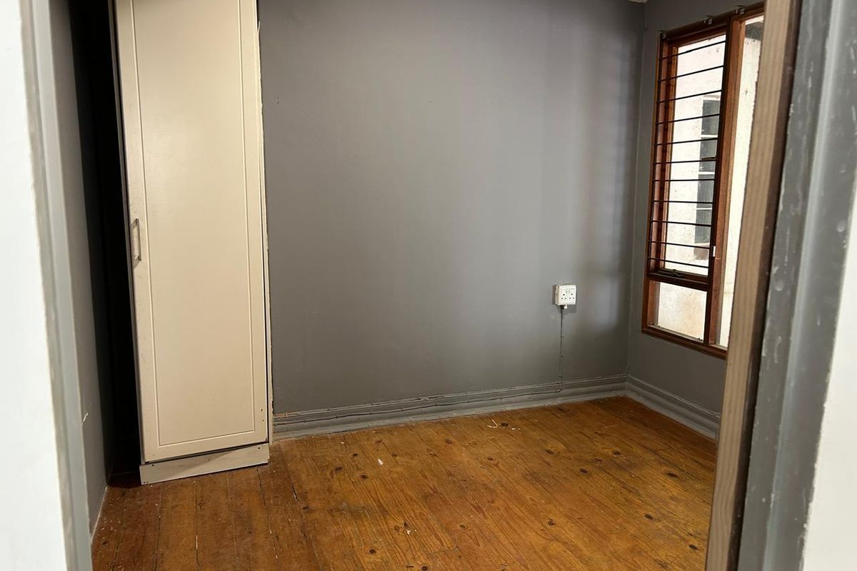 An empty bedroom featuring original timber flooring, a built-in cupboard, and a window fitted with security bars.